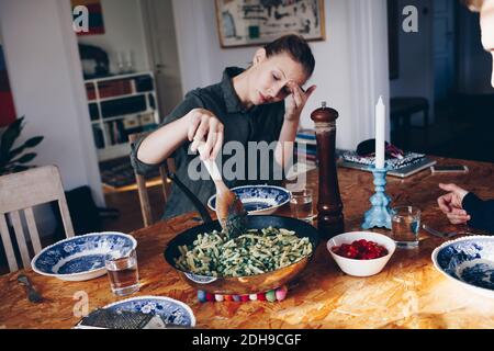 Femme tenant une cuillère en bois dans des pâtes sur la table à manger à accueil Banque D'Images