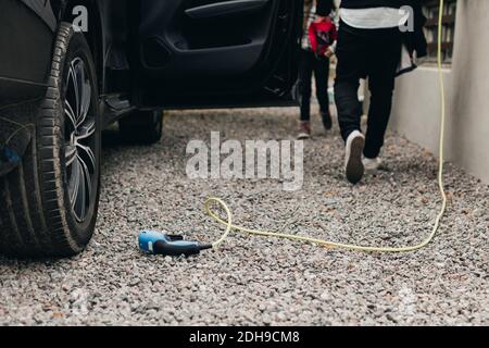 Section basse de l'homme avec fille à la charge de voiture électrique station Banque D'Images