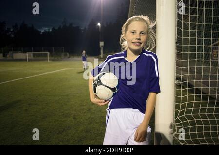 Portrait d'une fille heureuse tenant le ballon de football debout par le but publier sur le terrain Banque D'Images