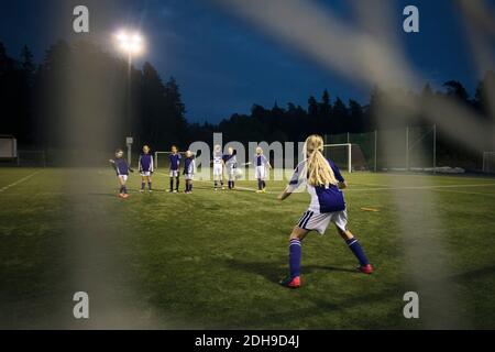 Les filles jouant au football vu de but post net sur le terrain contre le ciel Banque D'Images