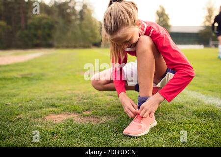 Une jeune fille se bousculant tout en nouant un cordonnet sur le terrain de football Banque D'Images