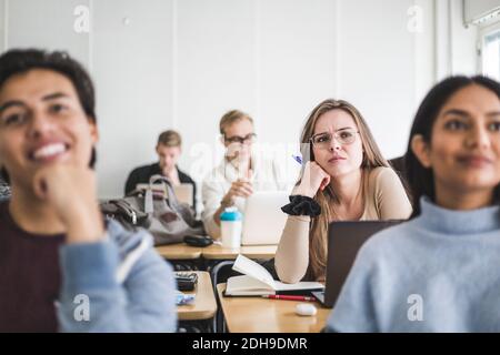 Jeune femme avec des amis à l'écoute pendant qu'elle est assise en classe Banque D'Images