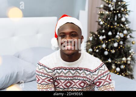 Portrait à la taille haute d'un sourire afro-américain posé dans un intérieur confortable, espace de copie. Joyeux homme beau en chapeau de Noël regardant l'appareil photo et smili Banque D'Images