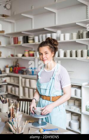 Portrait de jeune potter souriant de la forme de moulage sur l'argile pendant se tenir près de l'établi au magasin Banque D'Images