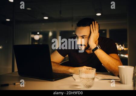 Homme d'affaires fatigué travaillant tard tout en regardant un ordinateur portable allumé bureau Banque D'Images