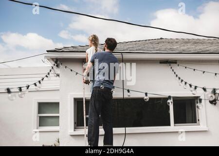 Vue arrière de l'homme avec sa fille grimpant sur l'échelle à maison Banque D'Images
