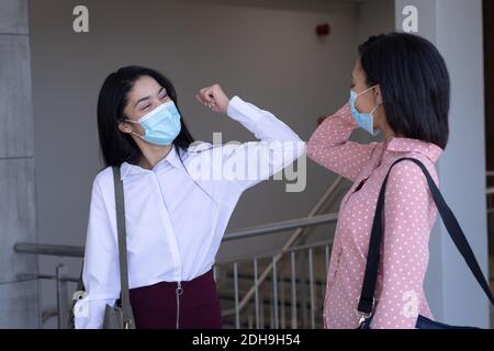 Deux femmes d'affaires portant un masque facial se saluent mutuellement en touchant des coudes dans un bureau moderne Banque D'Images
