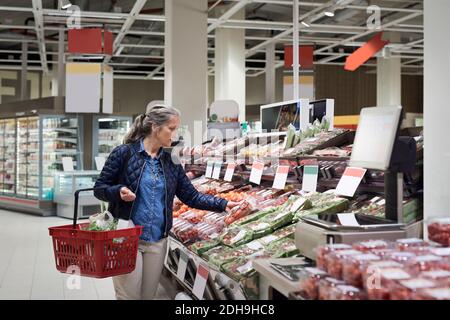 Femme mûre achetant aux légumes exposés dans le supermarché Banque D'Images