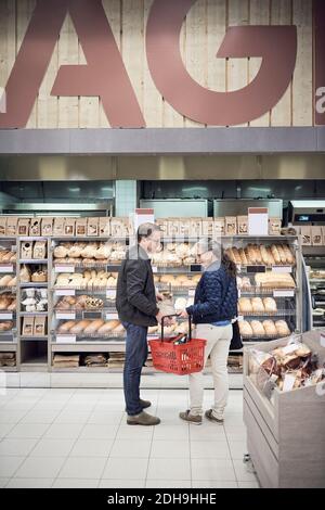 Couple d'âge mûr debout avec le panier contre la grille à pain au supermarché Banque D'Images