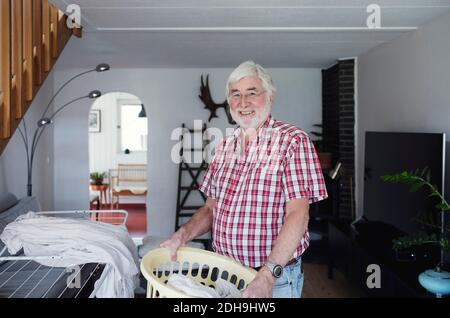 Portrait d'un homme âgé souriant tenant le panier à linge debout dans la salle de séjour Banque D'Images