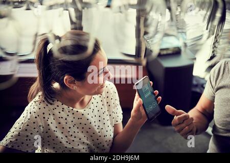 Vue en grand angle de la femme souriante montrant le smartphone à partenaire masculin dans le café Banque D'Images