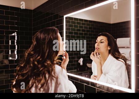 Femme adulte de taille moyenne regardant dans le miroir tout en appliquant un baume à lèvres Banque D'Images