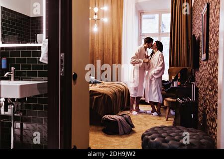 Couple embrassant tout en tenant des flûtes à champagne au lit à l'hôtel chambre Banque D'Images