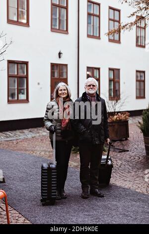 Portrait d'un couple senior debout sur le sentier avec les bagages contre hôtel Banque D'Images