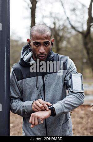 Portrait d'un athlète masculin confiant portant une montre et un bras intelligents bande en forêt Banque D'Images