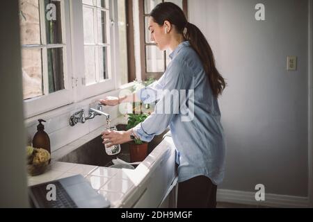 Vue latérale d'une femme d'affaires remplissant l'eau dans un pot à l'évier de cuisine Banque D'Images