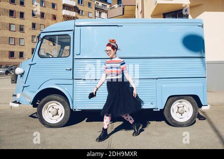 Jeune femme marchant dans un mini-minibus bleu dans la rue de la ville Banque D'Images