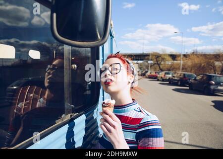 Jeune femme tenant le cône de crème glacée tout en se tenant par mini minibus dans la rue Banque D'Images