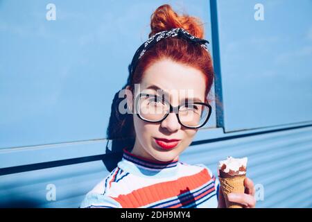 Portrait de la jeune femme à tête rouge tenant le cône de crème glacée contre mini-fourgonnette Banque D'Images