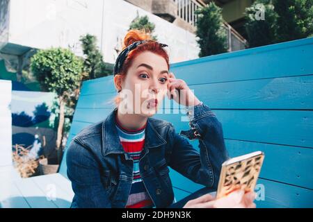 REDHEAD jeune femme prenant le selfie avec le téléphone mobile tout en étant assis sur banc Banque D'Images