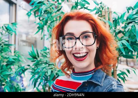 Portrait de jeune femme souriante à tête rouge contre la plante Banque D'Images