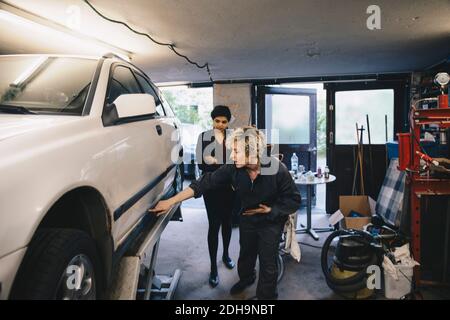 Une femme mécanique montre la voiture au client en mode automobile atelier de réparation Banque D'Images