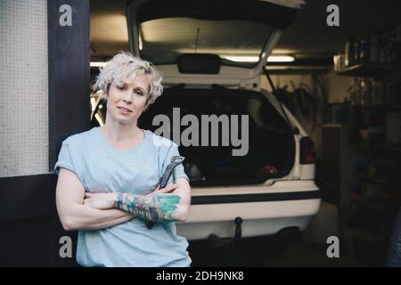 Portrait d'une femme confiante penchée sur la porte d'entrée de l'atelier de réparation automobile Banque D'Images