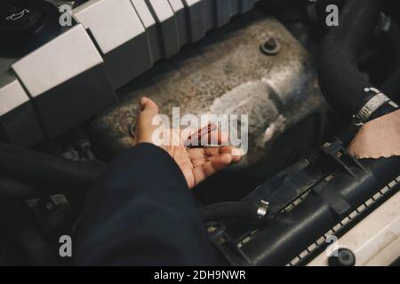 Main de mécanicien en train d'examiner l'huile dans le moteur de voiture à atelier de réparation automobile Banque D'Images