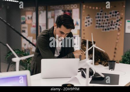 Jeune homme d'affaires utilisant un ordinateur portable tout en touchant un chien à son bureau bureau Banque D'Images