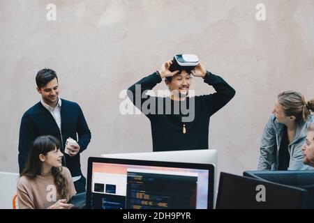 Un programmeur informatique masculin porte des lunettes VR lorsqu'il regarde ses collègues au bureau Banque D'Images
