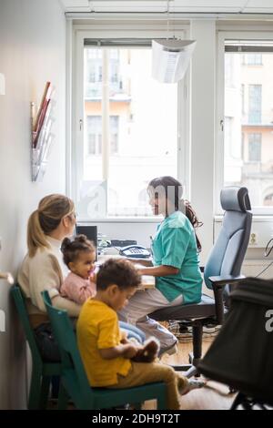 Pédiatre souriant parlant à la mère pendant que les enfants sont assis à la clinique Banque D'Images