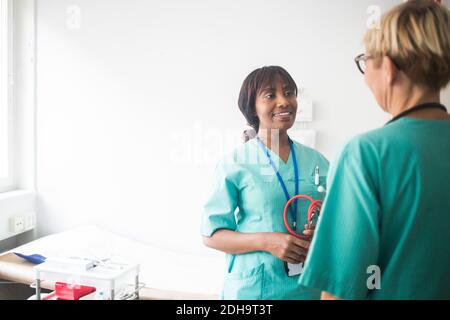 Femme pédiatre souriante avec des bangs parlant à un collègue mature pendant debout en clinique Banque D'Images