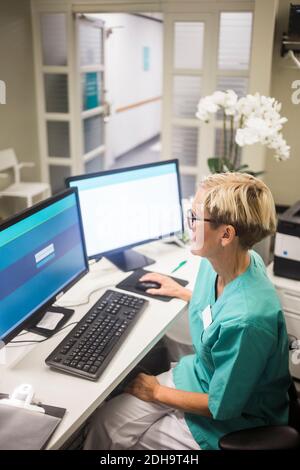 Vue en grand angle d'une femme mature travaillant sur un ordinateur assis à la clinique Banque D'Images