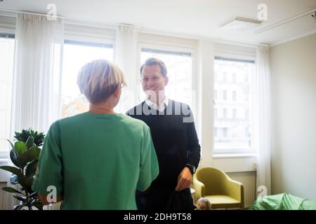 Sourire patient mûr secouant les mains avec une femme médecin debout en clinique Banque D'Images