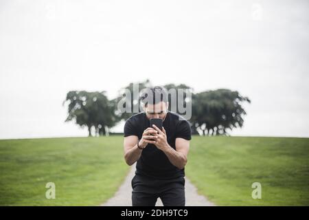 Jeune homme qui photographie à l'aide d'un smartphone tout en étant debout sur une piste de marche contre le ciel Banque D'Images