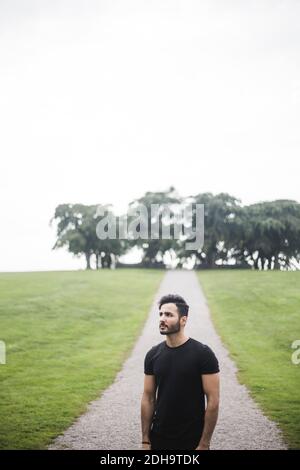 Jeune homme debout sur un sentier au milieu d'une terre herbeuse contre des arbres et le ciel Banque D'Images