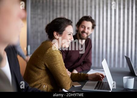 Une équipe d'affaires créative souriante assise avec un ordinateur portable à la table de conférence dans la salle de conseil Banque D'Images