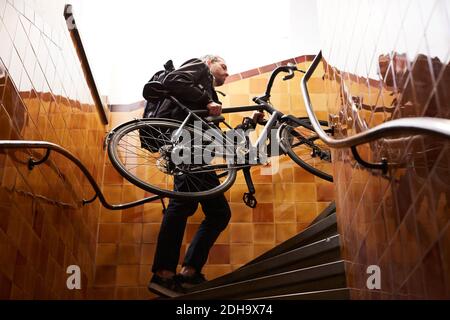 Vue basse sur un homme d'affaires transportant un vélo tout en grimpant étapes Banque D'Images