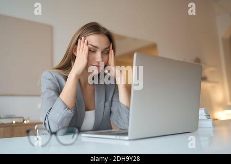 Coup de tête épuisé jeune femme prenant des lunettes, souffrent de la tension des yeux en raison du travail excessif de l'ordinateur. Femme de race mixte millénaire fatiguée et malsaine Banque D'Images