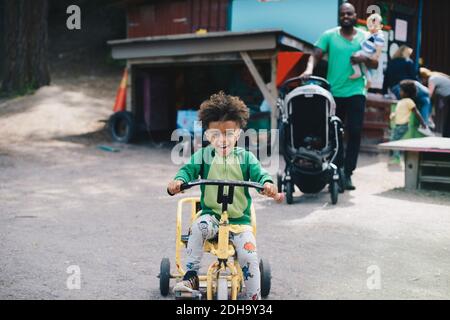 Joyeux garçon en tricycle pendant que le père et le frère marchent arrière-plan Banque D'Images