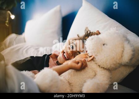Portrait d'un garçon heureux allongé avec un ours en peluche sur le lit à la maison Banque D'Images