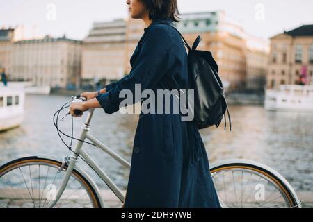Section médiane de la jeune femme avec vélo traversant la rivière dans la ville Banque D'Images