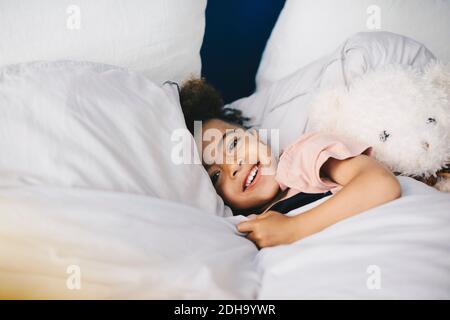 Portrait d'un garçon souriant dormant avec un ours en peluche sur le lit à la maison Banque D'Images