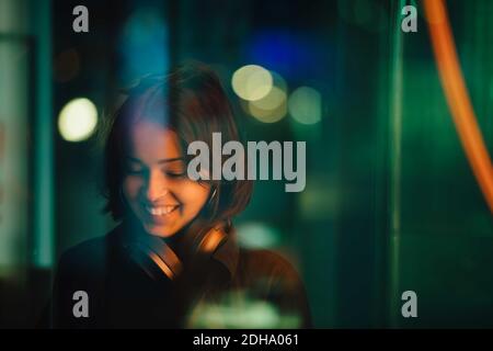 Femme souriante avec un casque dans la ville la nuit Banque D'Images