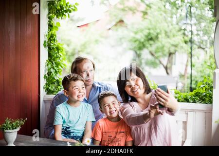 Mère prenant le selfie avec la famille dans le porche Banque D'Images