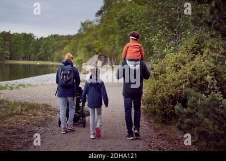 Vue arrière de la famille marchant sur le bord du lac pendant le coucher du soleil Banque D'Images