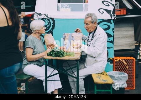 Homme et femme senior discutant des légumes tout en étant assis sur le marché en ville Banque D'Images