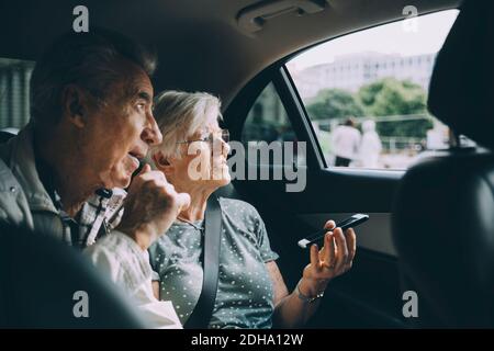 Femme âgée tenant un téléphone portable tout en étant assise avec un homme dedans voiture Banque D'Images