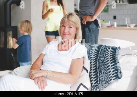 Portrait d'une femme âgée souriante assise sur un canapé avec sa famille en arrière-plan Banque D'Images