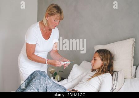 Grand-mère examinant la température de la petite-fille dans la chambre Banque D'Images